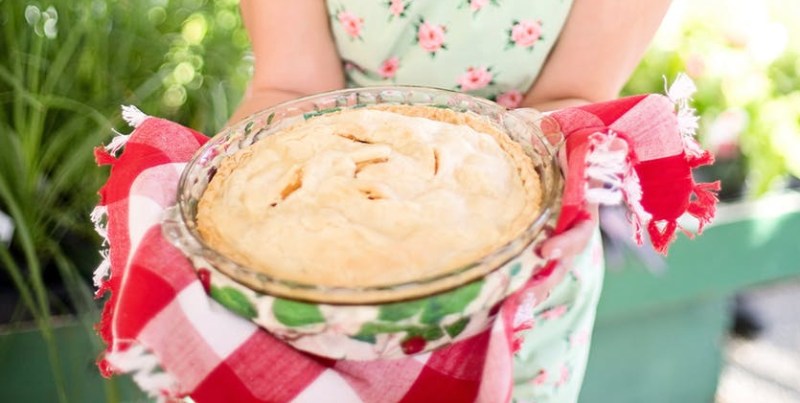 woman in pink white floral apron smiling while holding a white creme food during daytime